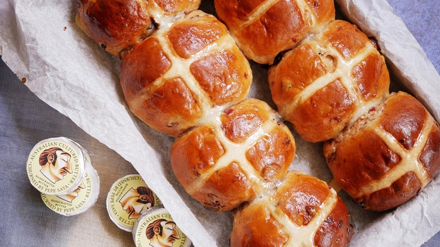 A tray of glazed white chocolate and cranberry hot cross buns served with butter