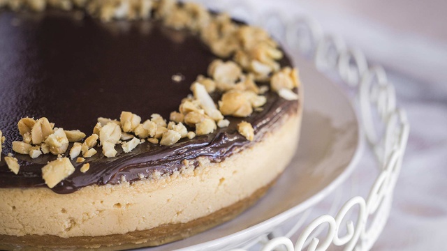 Peanut butter chocolate cheesecake shows brown tonal layers topped with peanuts
